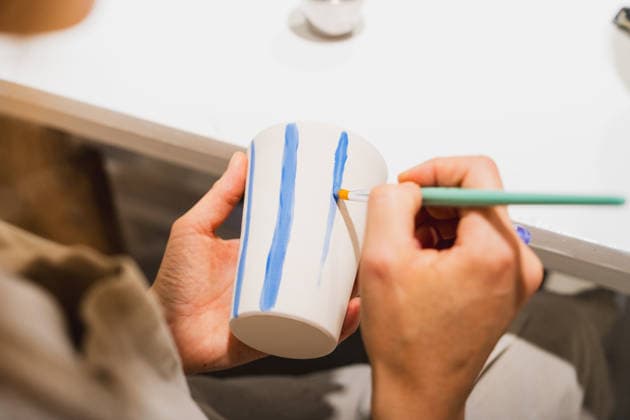 Woman paints blue stripes on a ceramic cup in a workshop model released, Symbolfoto property released, MRF02791