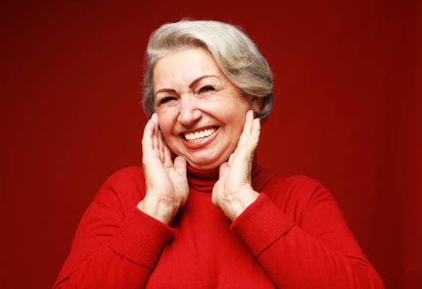 Eine fröhliche alte Frau in einem roten Pullover lacht und freut sich. Porträt vor rotem Hintergrund. A cheerful old woman in a red sweater laughs and rejoices. Portrait on a red background. Lifestyle and people concept. (License=RF) ,model released, Symbolfoto Copyright: xZoonar.com RaisaxKanarevax 25383400 ,model released, Symbolfoto ,property released