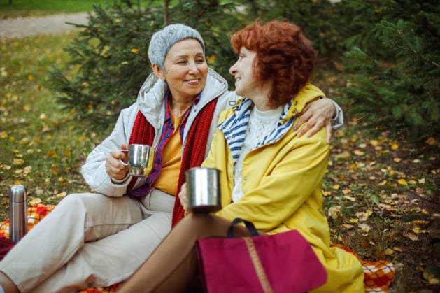 Zwei ältere Frauen sitzen auf einer karierten Decke im Wald, trinken Kaffee, unterhalten sich und haben Spaß. Two elderly women are sitting on a plaid blanket in the forest, drinking coffee, talking, having fun. Lifestyle concept. (License=RF) ,model released, Symbolfoto Copyright: xZoonar.com RaisaxKanarevax 25383415 ,model released, Symbolfoto ,property released