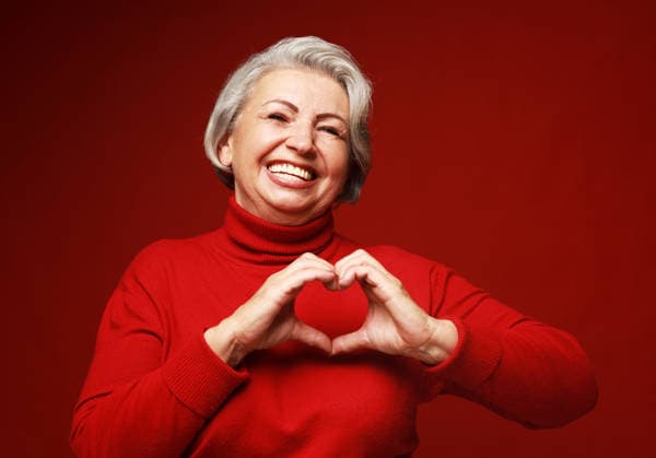 Ältere, grauhaarige Frau in einem roten Pullover, die verliebt lächelt und mit den Händen ein Herz formt. Senior grey-haired woman wearing red sweater smiling in love doing heart symbol shape with hands. Love and old people concept. (License=RF) ,model released, Symbolfoto Copyright: xZoonar.com RaisaxKanarevax 25383429 ,model released, Symbolfoto ,property released