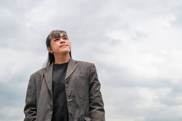 Horizontales Porträt einer asiatischen Person in einem Nadelstreifenanzug aus einem niedrigen Blickwinkel Horizontal low-angle photo of an Asian person in a dark pinstriped blazer suit jacket looking up and off-camera against a cloudy sky background with a slight smile. (License=RF) ,model released, Symbolfoto Copyright: xZoonar.com TonixRantalax 25391738 ,model released, Symbolfoto ,property released