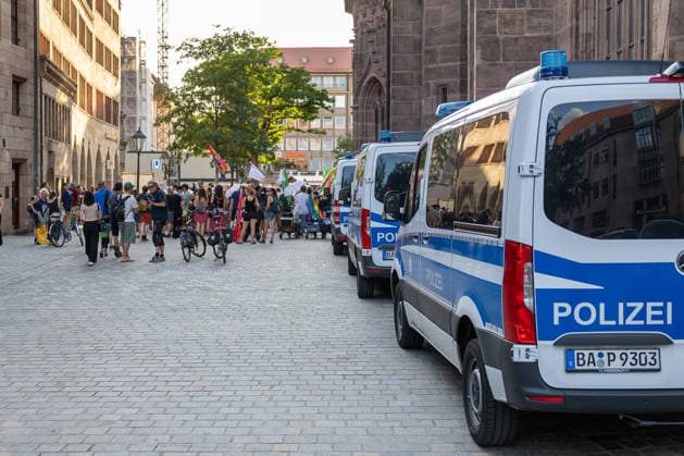 Polizeieinsatz bei Montagsdemo von Team Menschenrechte und Gegenprotesten, Nürnberg, 10.087.2026 Mehrere Einsatzfahrzeuge der Polizei stehen an der östlichen Seite der Lorenzkirche, während sich eine Gruppe von Demonstranten mit Fahnen und Transparenten versammelt. Passanten mit Fahrrädern beobachten das Geschehen auf dem Kopfsteinpflaster. Nürnberg Bayern Deutschland *** Police operation during the Monday demonstration by Team Menschenrechte and counter-protests, Nuremberg, 10 087 2026 Several police vehicles are parked on the east side of St. Lorenz Church, while a group of demonstrators carrying flags and banners gathers. Passersby on bicycles watch the scene unfold on the cobblestone street. Nuremberg, Bavaria, Germany 20260810-6V2A0609-M4000