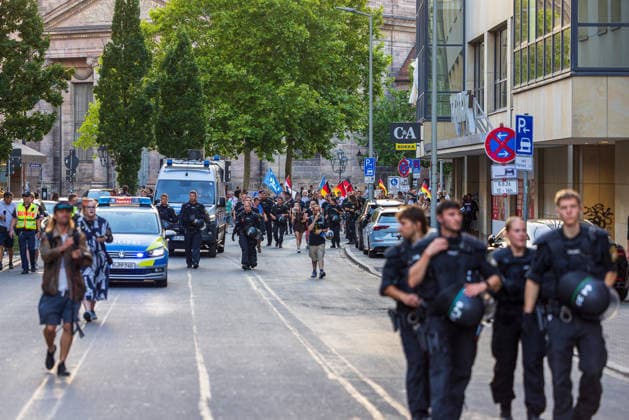 Polizeieinsatz bei Montagsdemo von Team Menschenrechte und Gegenprotesten, Nürnberg, 10.087.2026 Polizeikräfte in Schutzausrüstung begleiten einen Demonstrationszug mit Fahnen durch eine Innenstadtstraße. Fahrzeuge der Polizei sichern den Aufzug, während Passanten das Geschehen vom Straßenrand aus beobachten. Nürnberg Bayern Deutschland *** Police operation during the Monday demonstration by Team Menschenrechte and counter-protests, Nuremberg, 10 087 2026 Police officers in protective gear escort a demonstration march carrying flags through a downtown street. Police vehicles secure the procession, while passersby watch the events unfold from the sidewalk. Nuremberg, Bavaria, Germany 20260810-286A5031-M4000