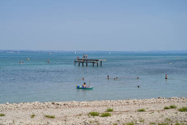 Lake Constance: Swimmers and water sports enthusiasts enjoy a sunny summer day on Lake Constance. People are swimming in the lake, riding in inflatable boats, and stand-up paddleboarding; others are standing on a swimming dock. In the background are sailboats and the opposite shore. Summer, heat, leisure, swimming, water sports, touri Copyright: xJOERANxSTEINSIEKx