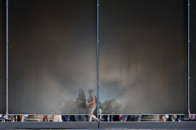 Ein temporaerer Gedenkort am Brandenburger Tor soll zum 65. Jahrestag des Mauerbaus an die deutsche Teilung erinnern (Foto vom 12.08.2026, im Bild: Menschen hinter der Installation). Die rund drei Meter hohe und 30 Meter lange Installation des Kuenstlers Hubertus Hamm auf dem Platz des 18. Maerz soll an die einstigen Grenzanlagen erinnern. Je nach Perspektive wirkt die Wand aus Aluminium lichtundurchlaessig oder transparent. (Siehe epd-Meldung vom 12.08.2026) EDITORIAL USE ONLY *** A temporary memorial site at the Brandenburg Gate is intended to commemorate the division of Germany on the 65th anniversary of the construction of the Berlin Wall. Photo taken on August 12, 2026, showing people behind the installation. The installation by artist Copyright: epd-bild ChristianxDitsch D26D0812MauerbauInstallation141307