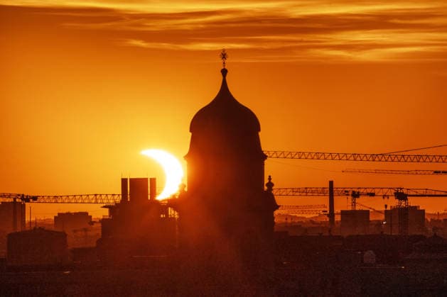 Partielle Sonnenfinsternis kurz nach ihrem Höhepunkt um 20:29 Uhr, Sonnensichel versinkt hinter dem Horizont neben dem Kirchturm von St. Wolfgang, Stadtteil Haidhausen, München, 12. August 2026 Deutschland, München, 12. August 2026, partielle Sonnenfinsternis kurz nach ihrem Höhepunkt um 20:28 Uhr, Sonnensichel versinkt neben dem markanten Zwiebelturm von St. Wolfgang in Haidhausen, der Mond schiebt sich vor die tiefstehende Sonne und deckt sie zu 89 Prozent ab, Sonnensichel kurz vor dem Sonnenuntergang um 20:32 Uhr, der Münchner Abendhimmel leuchtet in Orange, Blick von einem Hochhaus an der Rosenheimer Straße stadteinwärts, die katholische Pfarrkirche St. Wolfgang wurde 1920 eingeweiht, Astronomie, Sommer, Bayern, bayerisch, *** Pa