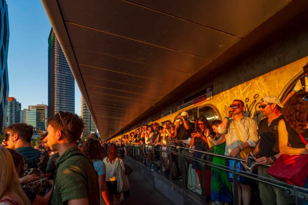 people with eclipse glasses watching partial solar eclipse on bridge Reichsbrücke, at subway U1 station entrance Donauinsel, view to Donaucity with DC Tower 1 Vienna 22. Donaustadt Wien Austria