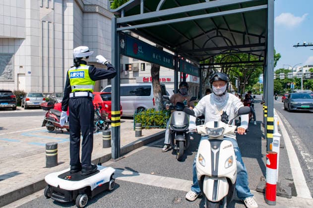 YONGKANG, CHINA - AUGUST 14: A robot traffic police officer advises riders to wear safety helmets at an intersection on August 14, 2026 in Yongkang, Jinhua, Zhejiang Province of China. Local authorities have launched a trial operation of robot traffic police to assist with road safety management.  Copyright: xVCGx 111659918415