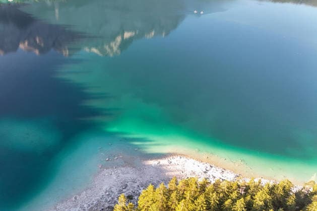Wetterfeature, Morgenstille am Eibsee: Unterhalb der Zugspitze liegt der See bei Grainau nahe Garmisch-Partenkirchen in den frühen Stunden noch ruhig und nahezu unberührt. Doch an heißen Sommertagen ändert sich das Bild häufig schon ab Mittag. Dann strömen zahlreiche Ausflügler und Urlauber an den durch soziale Medien weltweit bekannt gewordenen Bergsee. Der zunehmende Massentourismus sorgt regelmäßig für einen regelrechten Besucheransturm. Unter dem hohen Verkehrsaufkommen, zugeparkten Straßen und dem großen Andrang leiden zunehmend auch die Anwohner in Grainau und rund um den Eibsee. (Aufnahme mit einer Drohne) Grainau Bayern Deutschland Grainau *** Weather Feature, Morning Stillness at Eibsee. Nestled below the Zugspitze near Copyright: x xonw-imagesx xMariusxBullingx
