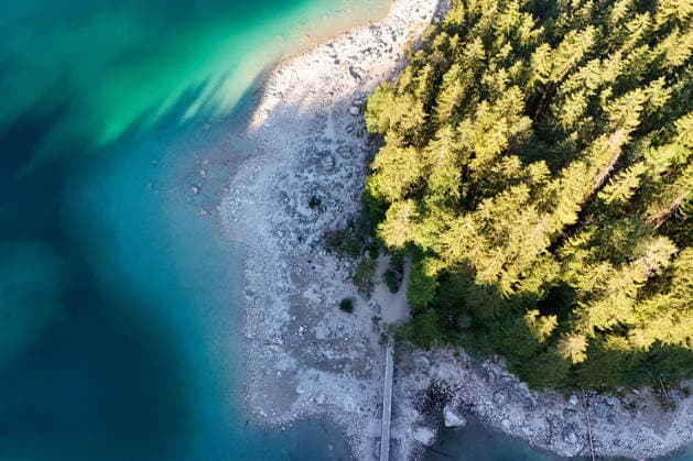 Wetterfeature, Morgenstille am Eibsee: Unterhalb der Zugspitze liegt der See bei Grainau nahe Garmisch-Partenkirchen in den frühen Stunden noch ruhig und nahezu unberührt. Doch an heißen Sommertagen ändert sich das Bild häufig schon ab Mittag. Dann strömen zahlreiche Ausflügler und Urlauber an den durch soziale Medien weltweit bekannt gewordenen Bergsee. Der zunehmende Massentourismus sorgt regelmäßig für einen regelrechten Besucheransturm. Unter dem hohen Verkehrsaufkommen, zugeparkten Straßen und dem großen Andrang leiden zunehmend auch die Anwohner in Grainau und rund um den Eibsee. (Aufnahme mit einer Drohne) Grainau Bayern Deutschland Grainau *** Weather Feature, Morning Stillness at Eibsee. Nestled below the Zugspitze near Copyright: x xonw-imagesx xMariusxBullingx