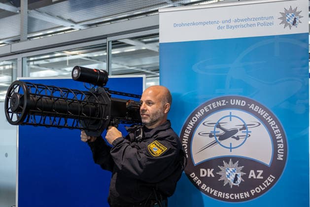 Drohnendetektion und -abwehr der Bayerischen Polizei, Flughafen Nürnberg, 14.08.2026 Ein Polizeibeamter demonstriert den Counter UAV Jammer HP 47+ PRO V7, ein tragbares, schultergestütztes Störsender-System zur Drohnenabwehr. Im Hintergrund ist das Logo des Drohnenkompetenz- und -abwehrzentrums der Bayerischen Polizei zu sehen. Nürnberg Flughafen Bayern Deutschland *** Drone Detection and Defense by the Bavarian Police, Nuremberg Airport, August 14, 2026 A police officer demonstrates the Counter UAV Jammer HP 47 PRO V7, a portable, shoulder-mounted jammer system for drone defense. In the background is the logo of the Bavarian Police’s Drone Competence and Defense Center. Nuremberg Airport, Bavaria, Germany 20260814-286A5303-M4000