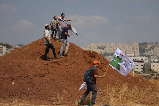 Activists Remove Flags From Beit Sahour Armed men stand on a mound of earth as activists carrying flags move nearby in Beit Sahour, east of Bethlehem in the occupied West Bank, on August 14, 2026. The activists said settlers had placed the symbols on the house after October 7, 2023, in what they described as an attempt to seize control of the property, and that settlers opened fire toward them as the items were removed, with no injuries reported. Bethlehem West Bank Palestinian Territories Copyright: xMosabxShawerx