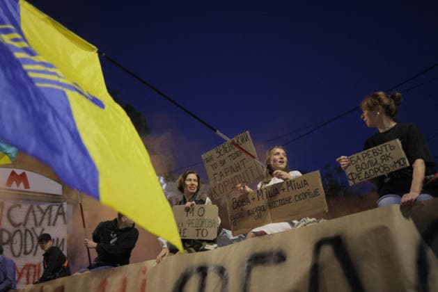 Kharkiv Protesters Demand Reinstatement of Defence Minister Fedorov - Ukraine Demonstrators sit atop a barrier and hold handwritten cardboard signs at Freedom Square (????? ???????) in Kharkiv, Ukraine, on August 14, 2026. One sign reads in Ukrainian ???? ??????????, ?? ?? ????? ?????? ????????? ( Mr. Zelensky, are you now the guarantor of corruption? ); another reads ?? ??? ???????? — ?? ?? ( The Ministry of Defence without Fedorov is not right ); a third reads ???? + ???? + ???? — ????? ??z?? ??????? ??????? (a vulgar political slogan linking the names); and a fourth reads ???????? ????, ?? ???????? ??? (partially legible); protesters gathered to demand the reinstatement of Mykhailo Fedorov as Minister of Defence, with a Ukrainian  Copyright: xTitovxYevhen ABACAx