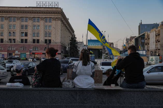 Kharkiv Protesters Demand Reinstatement of Defence Minister Fedorov - Ukraine Five people sit on a low stone parapet facing Freedom Square, one holding a Ukrainian flag aloft and another holding a small cardboard sign, as a billboard behind them reads ?????-????? ?????? ( Hero City Kharkiv ) in Kharkiv, Ukraine, on August 14, 2026. Participants gathered at Freedom Square (Ploshcha Svobody) on the 29th day of nationwide protests calling for the reinstatement of Mykhailo Fedorov as Minister of Defence, with approximately 500 Kharkiv residents joining the evening rally. Photo by Yevhen Titov ABACAPRESS.COM Kharkiv Kharkiv Oblast Ukraine  Copyright: xTitovxYevhen ABACAx