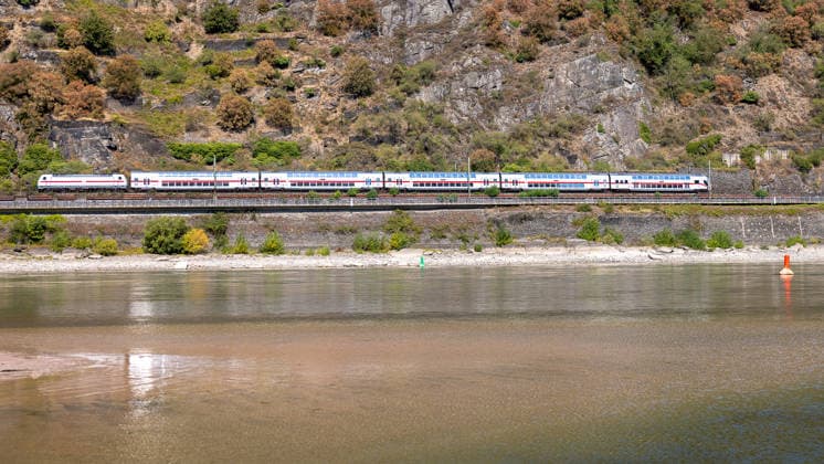 Niedrigwasser am Rhein nach langer Dürrephase, Kaub, 15.08.2026 Ein IC fährt entlang einer Felswand am Ufer, während der Fluss durch anhaltende Trockenheit deutlich niedrigen Wasserstand mit breiten freiliegenden Uferbereichen zeigt. Fahrwassertonnen markieren die verbliebene Fahrrinne. Kaub Rheinland-Pfalz Deutschland *** Low Water Levels on the Rhine Following a Long Drought, Kaub, August 15, 2026 An IC train passes along a rocky cliff on the riverbank, while the river, due to prolonged drought, shows significantly low water levels with wide stretches of exposed riverbank. Buoys mark the remaining navigable channel. Kaub, Rhineland-Palatinate, Germany 20260815-286A5756-M4000