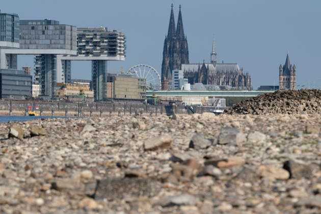Eine Teleaufnahme zeigt die markante Kölner Stadtkulisse mit den modernen Kranhäusern im Rheinauhafen und den gotischen Türmen des Kölner Doms im Hintergrund. Im unscharfen Vordergrund erstreckt sich das weitläufige, freigelegte Kiesel- und Steinufer des Rheins, das die Auswirkungen von extremem sommerlichem Niedrigwasser dokumentiert. *** A telephoto shot captures the prominent Cologne cityscape featuring the modern Kranhäuser buildings in the Rheinauhafen and the Gothic spires of the Cologne Cathedral in the background. In the blurred foreground, the vast, exposed pebble and stone bank of the Rhine illustrates the impact of extreme summer low water levels. Next to the cathedral, the white Nordrhein-Westfalen Deutschland, Germany 20260816-DSCF2155