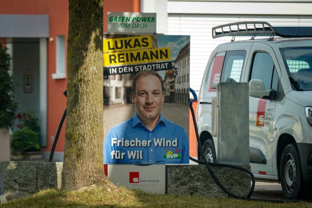 Schweiz: Politik, Wahlkampf in Wil (SG); Wahlplakat der Schweizerischen Volkspartei (SVP) mit Lukas Reimann als Kandidat für den Stadtrat von Wil. Das Plakat mit dem Slogan Frischer Wind für Wil steht unmittelbar neben einer Ladestation für Elektrofahrzeuge mit der Aufschrift Green Power vom Dach. Symbolbild für Kommunalpolitik, Wahlen, SVP, Elektromobilität und Energiewende. *** Swiss Politics, Election Campaign in Wil, SG: Election poster for the Swiss People’s Party (SVP) featuring Lukas Reimann as a candidate for the Wil City Council. The poster, bearing the slogan A Breath of Fresh Air for Wil, is located right next to an electric vehicle charging station with the inscription Green Power from the Roof —a symboli Copyright: xJOERANxSTEINSIEKx