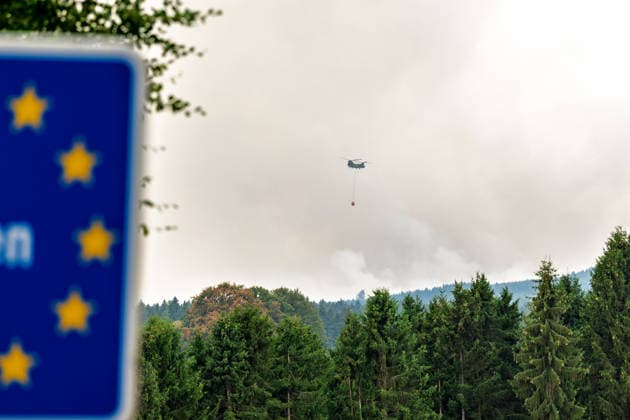 Waldbrand im Hohen Venn Blick von der deutsch-belgischen Grenze bei Kalterherberg - 15.08.26 Blick von Kalterherberg (Gemeinde Monschau) auf den Großbrand im Hohen Venn nahe der deutsch-belgischen Grenze. Im Vordergrund ein blaues Grenzschild im Hintergrund Rauchsäulen des Feuers und ein Löschhubschrauber mit Wasserbehälter im Anflug. Insgesamt zwei Löschhubschrauber sind im Einsatz und werfen jeweils rund 3.000 Liter Wasser ab. Der Hochmoorbrand hat bereits rund 2.000 Hektar Wald- und Moorgebiet erfasst, die tiefen Torfschichten begünstigen einen langanhaltenden Schwelbrand. Auf belgischer Seite laufen bereits Evakuierungen, für Teile Monschaus wird eine mögliche Räumung vorbereitet. Monschau Kalterherberg Nordrhein-Westfalen Copyright: xMarcxJohnx