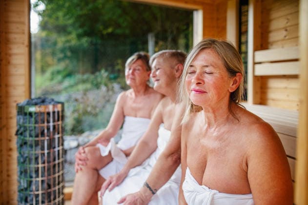 Senior women relaxing together in wooden sauna cabin with countryside view. Senior women relaxing together in wooden sauna cabin with countryside view. Wellness ritual. model released
