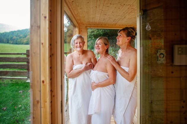 Senior women relaxing together in wooden sauna cabin with countryside view. Senior women relaxing together in wooden sauna cabin with countryside view. Wellness ritual. model released