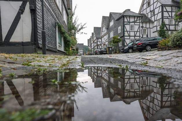 Wetterumschwung. Ein in den letzten Wochen eher seltenes Bild im Siegerland. Nach den trockenen heissen Tagen und Wochen startet die neue Woche nass und verhaeltnismaessig (verhältnismäßig) kuehl (kühl). Die Historische Altstadt von Freudenberg mit ihren Fachwerkhaeusern (Fachwerkhäusern). Die Haeuser (Häuser) spiegeln sich ein einer Pfuetze (Pfütze). Sommer im Siegerland am 17.08.2026 in Freudenberg Deutschland. *** Weather Change: A rare sight in the Siegerland region in recent weeks. After days and weeks of dry, hot weather, the new week is starting off wet and relatively cool. The historic old town of Freudenberg with its half-timbered houses. The haehouses are reflected in a puddle. Summer in the Siegerland region on August 17,