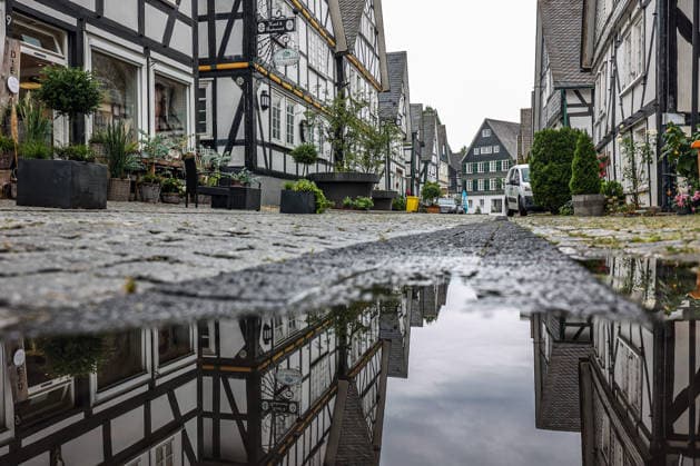 Wetterumschwung. Ein in den letzten Wochen eher seltenes Bild im Siegerland. Nach den trockenen heissen Tagen und Wochen startet die neue Woche nass und verhaeltnismaessig (verhältnismäßig) kuehl (kühl). Die Historische Altstadt von Freudenberg mit ihren Fachwerkhaeusern (Fachwerkhäusern). Die Haeuser (Häuser) spiegeln sich ein einer Pfuetze (Pfütze). Sommer im Siegerland am 17.08.2026 in Freudenberg Deutschland. *** Weather Change: A rare sight in the Siegerland region in recent weeks. After days and weeks of dry, hot weather, the new week is starting off wet and relatively cool. The historic old town of Freudenberg with its half-timbered houses. The haehouses are reflected in a puddle. Summer in the Siegerland region on August 17,