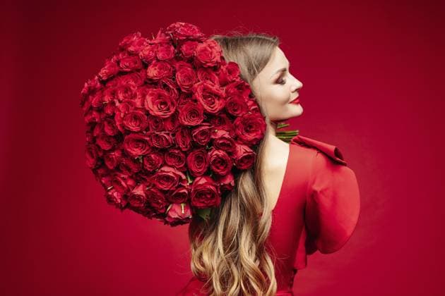 Studioporträt über der Schulter einer wunderschönen jungen Brünette mit leuchtenden Lippen im roten Kleid, die einen großen Strauß roter Rosen hält und vor rotem Hintergrund in die Kamera lächelt. Auf Rot isolieren Over shoulder studio portrait of gorgeous young brunette with bright lips in red dress holding big bouquet of red roses and smiling at camera over red background. Isolate on red Copyright: imageBROKER ViachaslauxKasko ibxiqx18580405.jpg ,model released, Symbolfoto ,property released