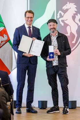 24.08.2026. Düsseldorf. (l-r) NRW-Ministerpräsident Hendrik Wüst und Ralf König bei der Verleihung des Verdienstordens des Landes Nordrhein-Westfalen anlässlich des 80. Landesgeburtstages. Ralf König hat als Autor und Comiczeichner mit seinen gesellschaftskritischen Cartoons Debatten über Sexualität, Religion, Politik und Rollenbilder angestoßen. Seit den 1980er Jahren hat er mit seinen Comics zur sexuellen Aufklärung beigetragen und Tabus aufgebrochen. Mit seinem Engagement für Kunstfreiheit und Menschenrechte hat er zudem gesellschaftliche Verantwortung übernommen. Düsseldorf Staatskanzlei Nordrhein-Westfalen Deutschland *** August 24, 2026, Düsseldorf NRW Minister President Hendrik Wüst and Ralf König at the award cerem