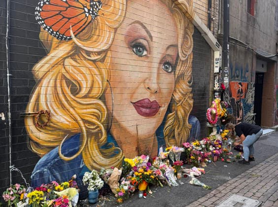 A woman arranges flowers at a memorial under a mural of Dolly Parton in Konxville, Tennessee on Friday, August 28, 2026.  TEN20260828102 AARONxJOSEFCZYK