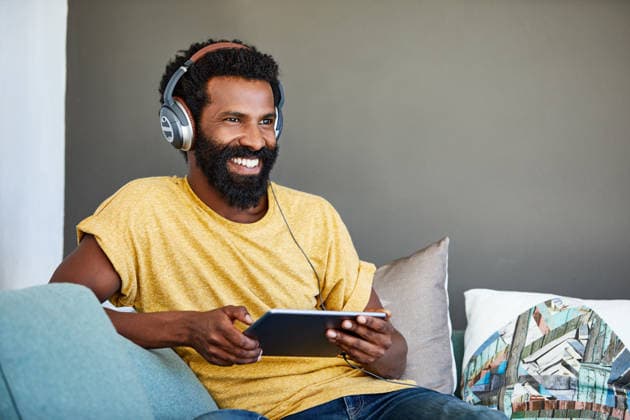 Headphones, relax and happy man with tablet on couch for music video, movie or thinking on weekend. Audio tech, home and African person with film idea, streaming service or listen to podcast online. model released property released Copyright: xx