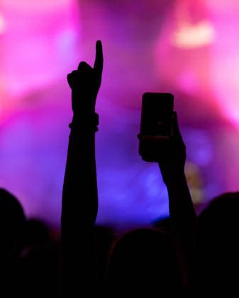A festivalgoer holds up one hand with her cell phone and the other hand with an outstretched finger during Ski Aggu s performance at the Glücksgefühle Festival at the Hockenheimring. Hockenheim, Baden-Württemberg, Germany