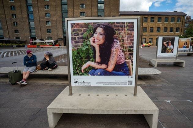 Amy Winehouse in Focus Free Exhibition Kings Cross in London, UK - 9 SEP2026. Two visitors seen sitting beside a portrait of the late singer in Granary Square, King’s Cross. Visitors view ‘Amy Winehouse: In Focus’, a free outdoor photography exhibition at Granary Square and King’s Boulevard in King’s Cross, London. The exhibition features defining and previously unseen photographs of the late singer, offering an intimate portrait of her life and career and marking 20 years since the release of her acclaimed album ‘Back to Black’. The exhibition runs from 1 September to 15 October 2026. London United Kingdom Copyright: xJamesxWilloughbyx xSOPAxImagesx JWILLOUGHBY_3326
