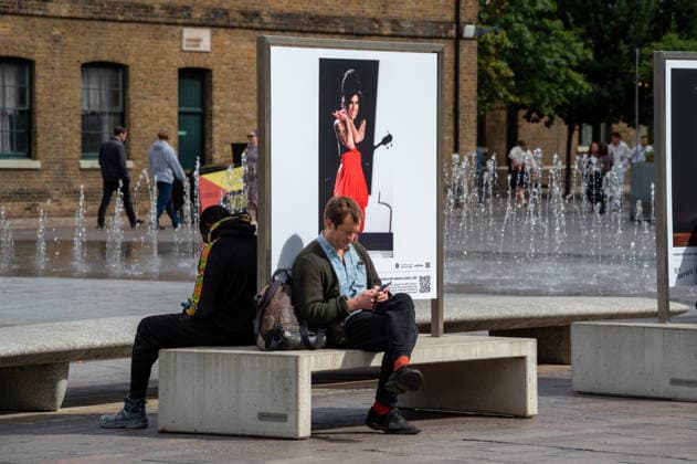 Amy Winehouse in Focus Free Exhibition Kings Cross in London, UK - 9 SEP2026. Two visitors seen sitting near a portrait of Amy Winehouse displayed as part of the ‘Amy Winehouse. Visitors view ‘Amy Winehouse: In Focus’, a free outdoor photography exhibition at Granary Square and King’s Boulevard in King’s Cross, London. The exhibition features defining and previously unseen photographs of the late singer, offering an intimate portrait of her life and career and marking 20 years since the release of her acclaimed album ‘Back to Black’. The exhibition runs from 1 September to 15 October 2026. London United Kingdom Copyright: xJamesxWilloughbyx xSOPAxImagesx JWILLOUGHBY_3336