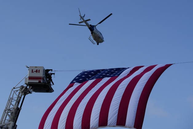 (260912) -- SURREY, Sept. 12, 2026 -- A helicopter flies over a large U.S. national flag during a commemoration marking the 25th anniversary of the 9 11 attacks in Surrey, British Columbia, Canada, Sept. 11, 2026. About 400 people from Canada and the United States gathered here on Friday to commemorate the 9 11 attacks on the 25th anniversary. (Photo by Xinhua) CANADA-SURREY-9 11 ATTACKS-COMMEMORATION LiangxSen 