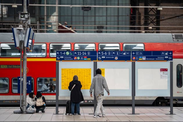 A woman traveling stands on Platform 6 7 and looks at the schedule while a beggar approaches her; in the background is the RB81 commuter train to Bad Oldesloe, Deutsche Bahn AG, Hamburg Central Station, Hamburg, Germany