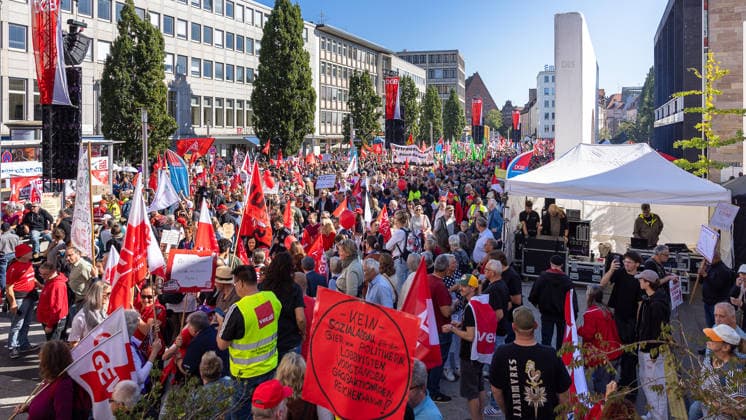 DGB Bavaria Hard Earned Large Rally, Nuremberg, September 26, 2026 Numerous participants in the DGB Hard Earned rally gather at the Kornmarkt for a protest featuring union flags and banners. A speaker addresses the crowd from a covered stage, while demonstrators hold up signs with messages against social injustice. Nuremberg, Bavaria, G 20260926-286A9175-M4000