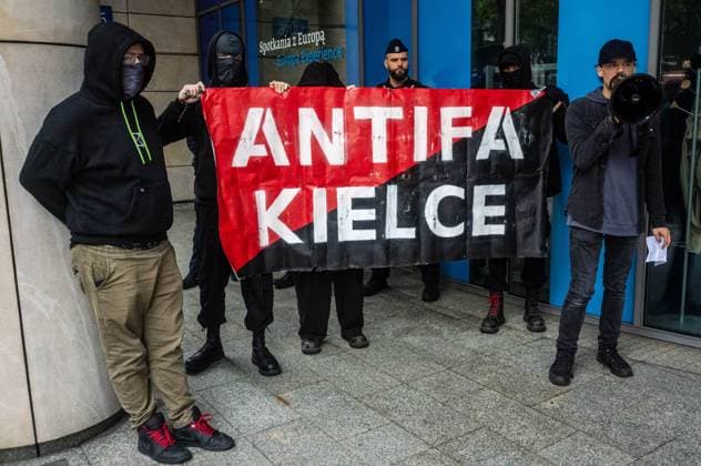 September 26, 2026, Warsaw, Mazovia, Poland: Masked antifa activists hold a banner next to a protester speaking through a megaphone..Left-wing antifascist activists gather outside the European Union Commission building in Warsaw to protest against the Chat Control 1.0 legislation recently revived by the European Parliament. The legislation allows for the mass scanning of messages belonging to every European Union citizen for Child Sexual Abuse Material (CSAM) in the name of protecting children s rights and combating pedophilia. The activists, however, believe rights to privacy and the foundations of free speech are being trampled upon, especially with talks due to resume regarding the far more dangerous Chat Control 2.0 bill, which aims - ZUMAs197 20260926_aaa_s197_186 Copyright: xNeilxMiltonx