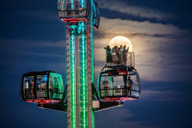 The full moon, also known as the Harvest Moon, shines behind the SkyLift at Oktoberfest; festivalgoers in the gondolas and on the open grounds take photos with their smartphones, Munich, September 26, 2026, Germany, Munich, September 26, 2026—The full mo