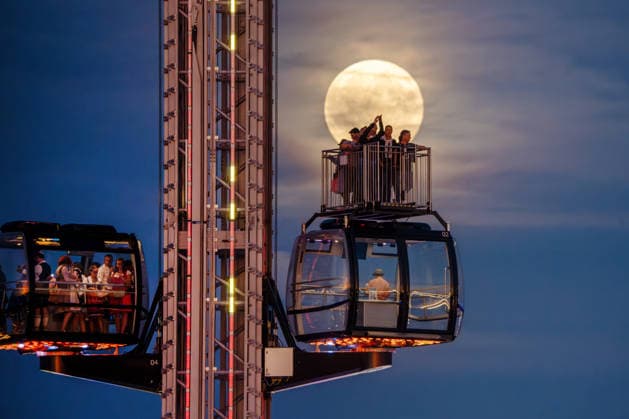 The full moon, also known as the Harvest Moon, shines behind the SkyLift at Oktoberfest; festivalgoers in the gondolas and on the open grounds take photos with their smartphones, Munich, September 26, 2026, Germany, Munich, September 26, 2026: The full mo
