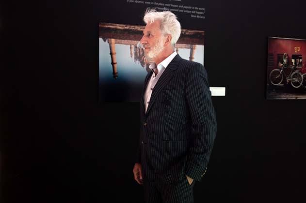 Tübingen, Gysis Encounters at the New Art Museum with Rufus Beck, September 28, 2026; a side profile portrait of Rufus Beck in front of photographs by photographer Steve McCurry