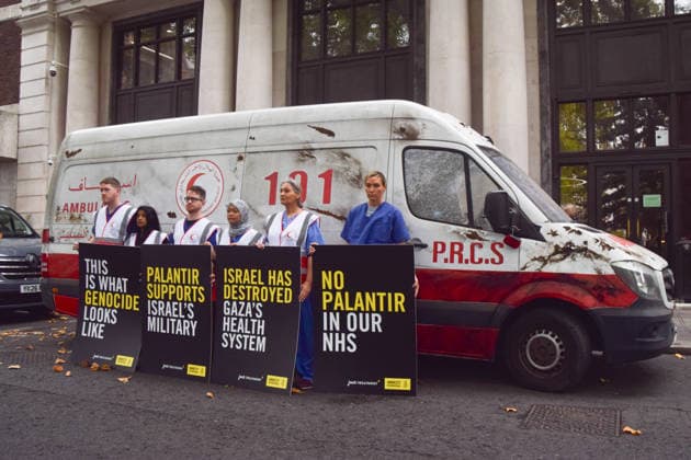 September 30, 2026, London, England, United Kingdom: Healthcare professionals stand with placards next to a van made to look like a heavily damaged Gaza ambulance as Amnesty International UK and Just Treatment stage a protest outside Palantir headquarters in Soho Square. The campaigners are calling on the UK Government not to extend its NHS contract with the US tech company. London United Kingdom - ZUMAv130 20260930_zip_v130_008 Copyright: xVukxValcicx