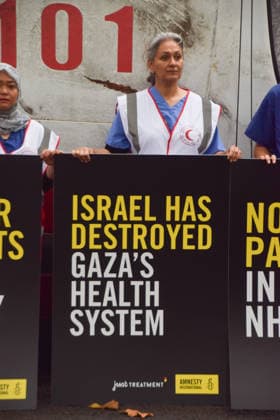 September 30, 2026, London, England, United Kingdom: Healthcare professionals stand with placards next to a van made to look like a heavily damaged Gaza ambulance as Amnesty International UK and Just Treatment stage a protest outside Palantir headquarters in Soho Square. The campaigners are calling on the UK Government not to extend its NHS contract with the US tech company. London United Kingdom - ZUMAv130 20260930_zip_v130_013 Copyright: xVukxValcicx