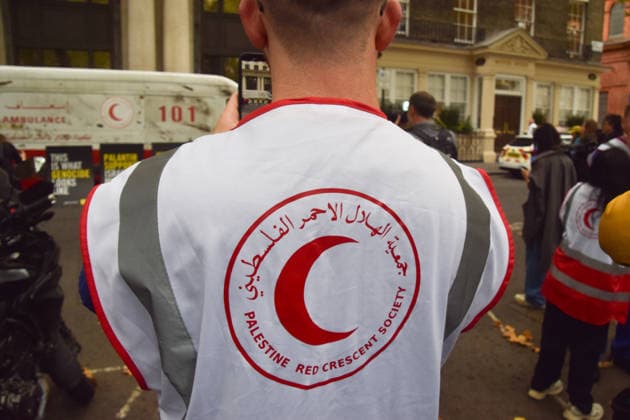September 30, 2026, London, England, United Kingdom: A healthcare professional wears a Palestine Red Crescent Society vest and a van made to look like a heavily damaged Gaza ambulance is parked outside Palantir headquarters in Soho Square as Amnesty International UK and Just Treatment stage a protest calling on the UK Government not to extend its NHS contract with the US tech company. London United Kingdom - ZUMAv130 20260930_zip_v130_020 Copyright: xVukxValcicx