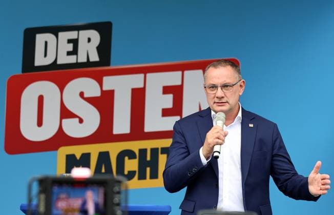Enjoying a Bratwurst with Haseloff and Chrupalla, October 1, 2026, Doellstaedt, AfD event at Kiesling Roofing; enjoying a bratwurst with state parliament member Daniel Haseloff (AfD) and AfD national spokesperson Tino Chrupalla. Pictured: Tino Chrupalla giving a speech on stage, with the phrase The East is doing it in the background.