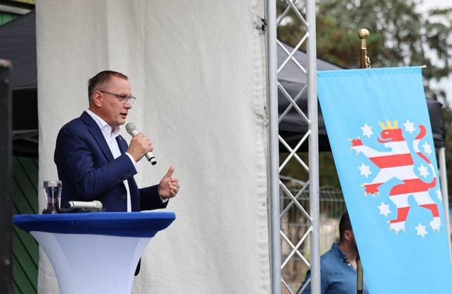 Enjoying a Bratwurst with Haseloff and Chrupalla, October 1, 2026, Doellstaedt, AfD event at Kiesling Roofing; enjoying a bratwurst with State Parliament Representative Daniel Haseloff (AfD) and AfD National Spokesperson Tino Chrupalla. Pictured: Tino Chrupalla giving a speech on stage; a flag featuring the Thuringian Lion hangs on the right.