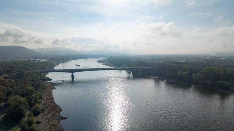 Niedrigwasser legt Uferbereiche des Rheins in Bonn frei Bonn, 02.10.2026: Drohnenaufnahme des Rheins bei der Südbrücke in Bonn. Auf beiden Seiten des Flusses sind großflächige, trockengefallene Uferbereiche zu sehen. Über dem Rhein und der umliegenden Landschaft liegt leichter Nebel. Im Hintergrund zeichnet sich das Siebengebirge nur schwach im Dunst ab. Die Südbrücke, offiziell Konrad-Adenauer-Brücke, verbindet die Bonner Stadtteile Gronau und Beuel und führt die Bundesstraße 56 über den Rhein. Die 1972 eröffnete Brücke gehört zu den wichtigen Rheinquerungen im Bonner Stadtgebiet. Die Aufnahme zeigt die aufgrund des niedrigen Wasserstands deutlich erweiterten Uferflächen des Rheins. Bonn Ramersdorf Nordrhein-Westfalen Deut