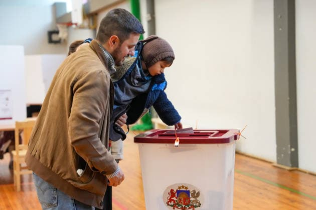 (261003) -- RIGA, Oct. 3, 2026 -- A voter casts a ballot with his child at a polling station in Riga, Latvia, Oct. 3, 2026. Voting in the Latvian parliamentary election began on Saturday morning, with 1,428 candidates vying for 100 seats in the 15th Saeima, Latvia s parliament. (Photo by Xinhua) LATVIA-RIGA-PARLIAMENTARY ELECTION EdijsxPalens 
