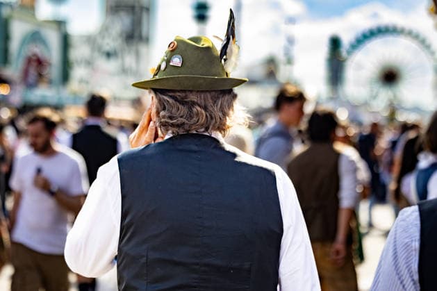 Oktoberfest 2026 in Munich, October 4, 2026: A man in traditional costume and a traditional hat stands among the visitors on the festival grounds. He is holding his left hand to his ear while talking on the phone. The 191st Oktoberfest took place in 2026 from September 19 to Octo