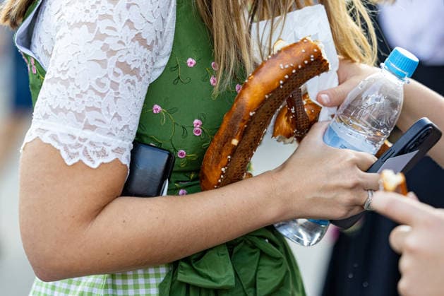 Oktoberfest 2026 in Munich, October 4, 2026: A female visitor wearing a dirndl holds a pretzel and a bottle of water on the festival grounds. The 191st Oktoberfest took place from September 19 to October 4, 2026, at the Theresienwiese. Munich’s Oktoberfest is one of the largest folk festivals in the world and attracts millions of v