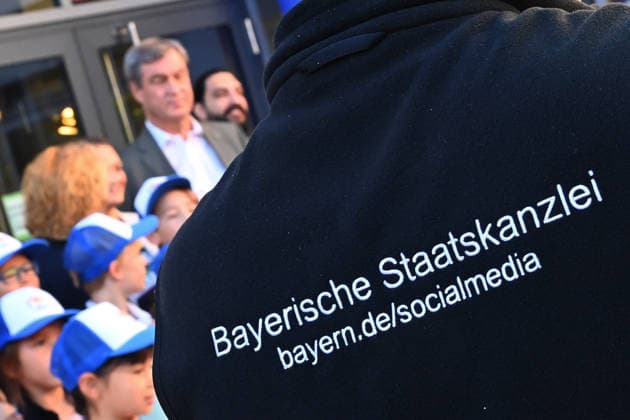 The back of a person with the words Bavarian State Chancellery, Social media takes center stage at a school visit with Minister President Markus Söder Markus SÖDER, Minister President of Bavaria and CSU